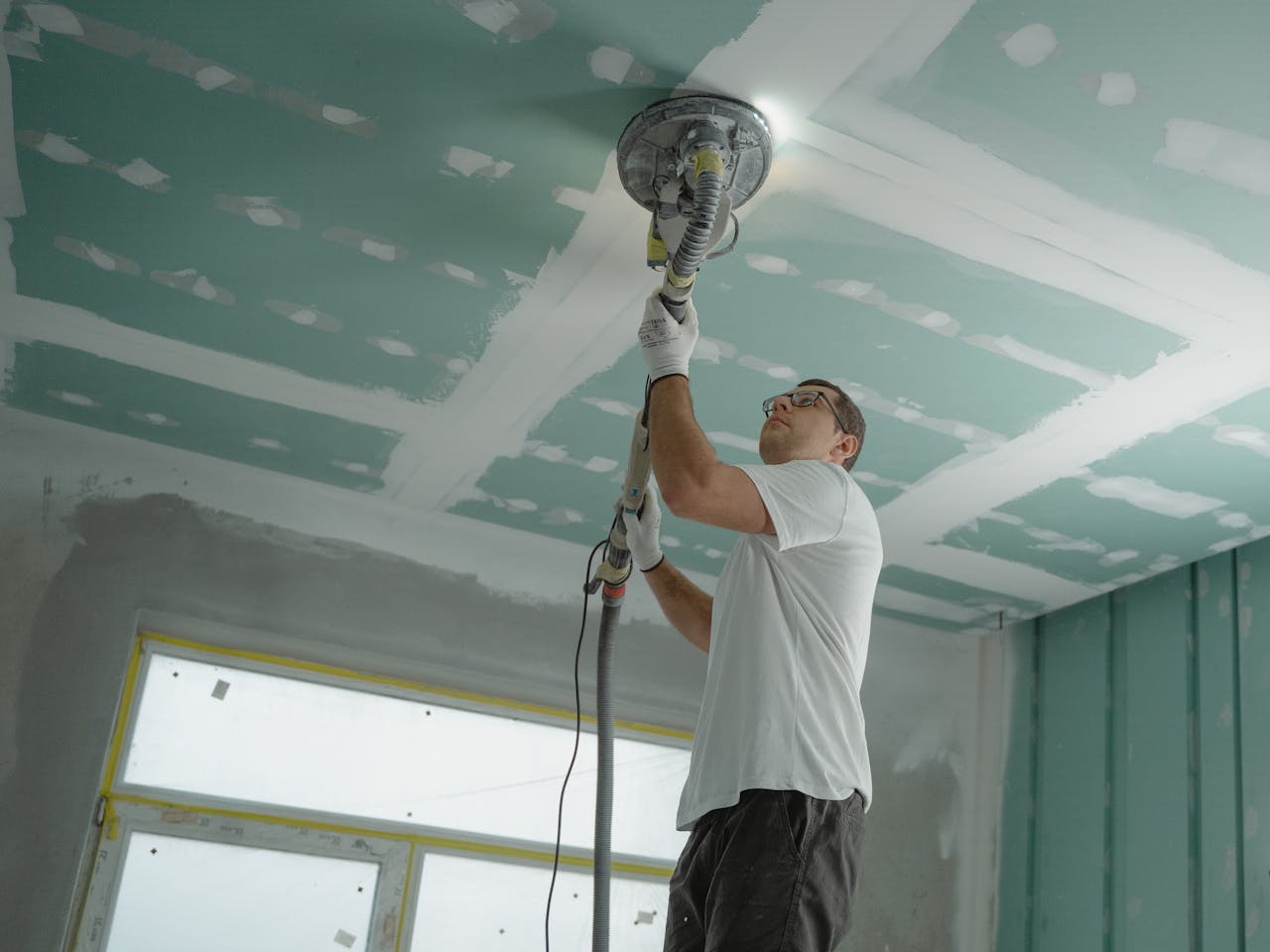 Home A professional worker sanding the ceiling during a home renovation project. Indoor construction setting.